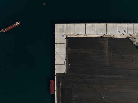 Aerial view of a concrete industrial pier and a cargo ship navigating dark blue waters in the harbor of Augusta Sicily Italy. Aerial view of a concrete industrial pier and a cargo ship navigating dark blue waters in the harbor of Augusta Sicily Italy.