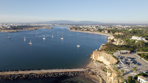 Aerial view of the coastal town of Ferragudo featuring boats anchored in the bay rocky cliffs and a parking area near the shoreline in Ferragudo Faro District Portugal.
