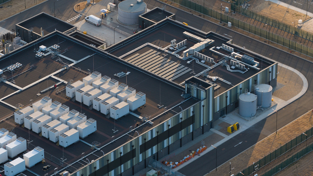 Aerial view of a modern data center facility featuring rows of white cooling units on the roof industrial storage tanks and a secure perimeter in Bracknell England United Kingdom.