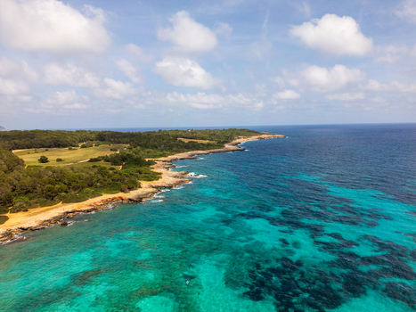 Aerial view of the rocky coastline and turquoise waters of the Mediterranean Sea under a blue sky with white clouds in Sa Coma Balearic Islands Spain. Aerial view of the rocky coastline and turquoise waters of the Mediterranean Sea under a blue sky with white clouds in Sa Coma Balearic Islands Spain.