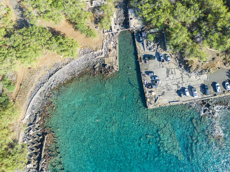 Aerial view of Mahukona Beach Park featuring crystal clear turquoise water a concrete pier with people and parked cars and lush green trees in Waimea Hawaii United States.