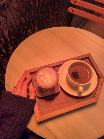 View of a person s hand resting on a marble table next to two cups of coffee on a wooden tray under warm orange lighting in Beylikduzu Istanbul Turkiye. View of a person s hand resting on a marble table next to two cups of coffee on a wooden tray under warm orange lighting in Beylikduzu Istanbul Turkiye.