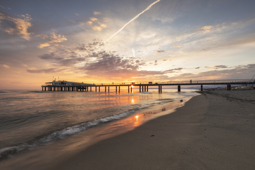 View of the Lido di Camaiore pier extending into the sea at sunset with people walking along the deck and waves washing onto the sandy beach Lido di Camaiore Tuscany Italy.