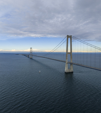 Aerial view of the Great Belt Bridge spanning across the blue sea under a cloudy sky with a small sailboat in Denmark. Aerial view of the Great Belt Bridge spanning across the blue sea under a cloudy sky with a small sailboat in Denmark.