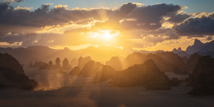 Aerial view of dramatic sandstone rock formations and desert landscape under a golden sunset with sun rays piercing through clouds in Tabuk Tabuk Province Saudi Arabia.