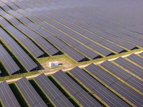Aerial view of a large solar farm with rows of photovoltaic panels and a central electrical substation in Poland.