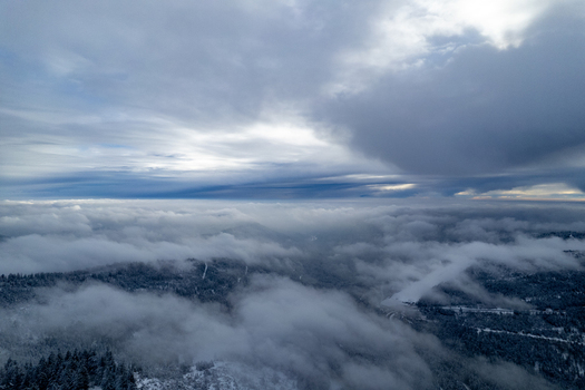 Aerial view of the snow covered landscape surrounding Mummelsee with dense low hanging clouds and fog drifting over the forested hills in Seebach Baden Wurttemberg Germany. Aerial view of the snow covered landscape surrounding Mummelsee with dense low hanging clouds and fog drifting over the forested hills in Seebach Baden Wurttemberg Germany.