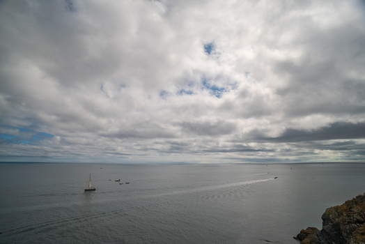 View of a sailboat and small boats on the Fowey River with a rocky coastline under a cloudy sky in Fowey Cornwall United Kingdom. View of a sailboat and small boats on the Fowey River with a rocky coastline under a cloudy sky in Fowey Cornwall United Kingdom.