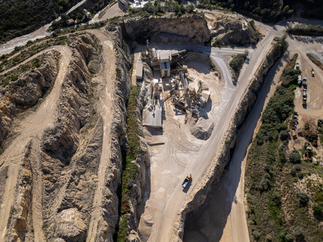 Aerial view of a stone quarry featuring heavy machinery gravel piles and winding access roads carved into the rocky landscape Teulada Valencian Community Spain.