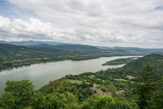 View of the Danube River winding through lush green hills under a cloudy sky in Budapest Hungary.