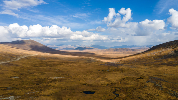 Aerial view of Deosai National Park featuring vast golden brown plateaus rolling hills a winding dirt road and small water pools in Skardu Gilgit Pakistan.