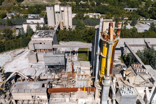 Aerial view of the Sacci S.P.A. cement factory featuring large industrial silos metal pipes and concrete structures surrounded by trees in Castelraimondo Marche Italy. Aerial view of the Sacci S.P.A. cement factory featuring large industrial silos metal pipes and concrete structures surrounded by trees in Castelraimondo Marche Italy.