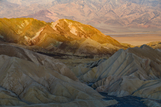 View of the rugged colorful badlands of Death Valley National Park s backcountry featuring eroded golden hills under soft light in Death Valley California United States.