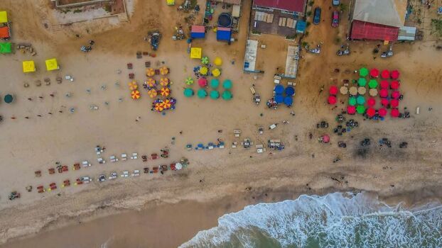 Aerial view of a vibrant beach featuring rows of colorful umbrellas scattered beach chairs and people relaxing on the sand near the ocean waves in Ghana. Aerial view of a vibrant beach featuring rows of colorful umbrellas scattered beach chairs and people relaxing on the sand near the ocean waves in Ghana.