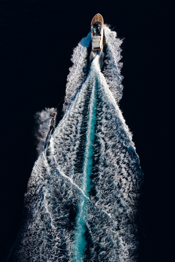 Aerial view of a motorboat towing a water skier creating a long white wake in the deep blue waters near Le Trayas in Saint Raphael Provence Alpes Cote d Azur France. Aerial view of a motorboat towing a water skier creating a long white wake in the deep blue waters near Le Trayas in Saint Raphael Provence Alpes Cote d Azur France.