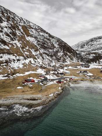 Aerial view of Grotfjord with traditional red houses nestled at the foot of snow dusted mountains along the rocky coastline Tromvik Troms Norway. Aerial view of Grotfjord with traditional red houses nestled at the foot of snow dusted mountains along the rocky coastline Tromvik Troms Norway.