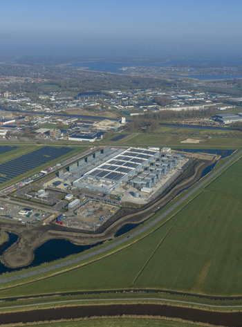 Aerial view of digital data center facility with solar panels on the roof surrounded by green fields and canals under a clear blue sky Netherlands. Aerial view of digital data center facility with solar panels on the roof surrounded by green fields and canals under a clear blue sky Netherlands.