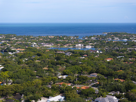 Aerial view of lush green residential neighborhoods with luxury homes and canals near the blue ocean in Coral Gables Florida United States.