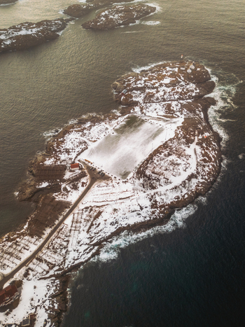 Aerial view of snow dusted islands meet the turbulent sea a stark contrast under the muted sky Henningsv&aelig;r Nordland Norway.