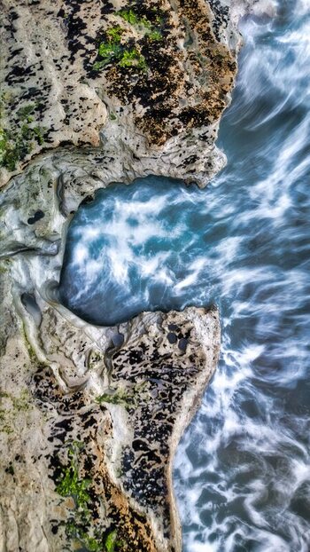 Aerial view of the rugged coastline featuring textured rock formations and swirling ocean waves crashing against the shore in Waiiti Taranaki Region New Zealand.
