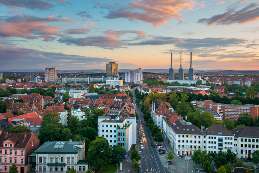 Aerial view of the cityscape of Hannover with historic rooftops urban streets and industrial chimneys under a colorful sunset sky in Hannover Germany.