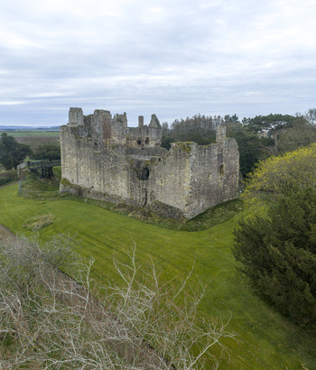 Aerial view of the historic ruins of Dirleton Castle and Gardens surrounded by lush green lawns and dense trees under a cloudy sky in Dirleton Scotland United Kingdom. Aerial view of the historic ruins of Dirleton Castle and Gardens surrounded by lush green lawns and dense trees under a cloudy sky in Dirleton Scotland United Kingdom.