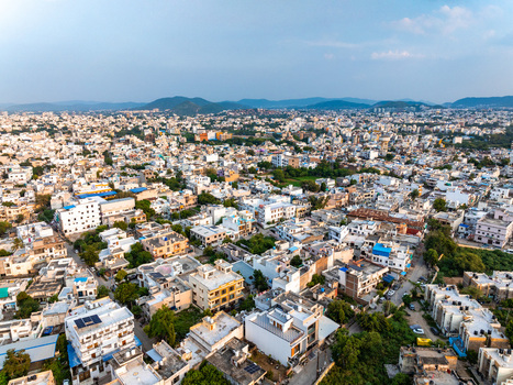 Aerial view of the dense urban landscape of Udaipur featuring white buildings rooftops and distant hills under a clear sky in Udaipur Rajasthan India. Aerial view of the dense urban landscape of Udaipur featuring white buildings rooftops and distant hills under a clear sky in Udaipur Rajasthan India.
