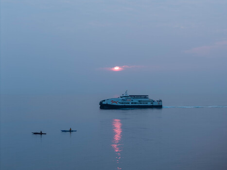 Aerial view of a ferry crossing the calm sea near two small traditional outrigger boats during a soft sunset in Dumaguete City Negros Island Region Philippines. Aerial view of a ferry crossing the calm sea near two small traditional outrigger boats during a soft sunset in Dumaguete City Negros Island Region Philippines.