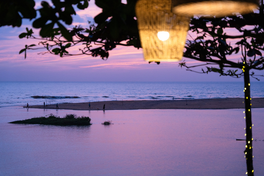 View of a serene beach at twilight with purple sky silhouettes of people on the sand and a glowing woven lantern in the foreground in Galle Southern Province Sri Lanka.