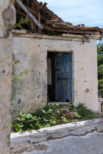 View of an abandoned stone house with a weathered blue door and a broken tiled roof in Qeparo Fshat Vlore County Albania. View of an abandoned stone house with a weathered blue door and a broken tiled roof in Qeparo Fshat Vlore County Albania.
