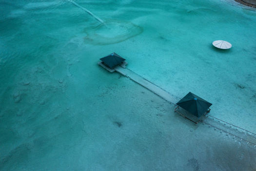 Aerial view of a weathered pier stretching into the tranquil turquoise waters contrasting with the stark white of a solitary parasol Arad South District Israel. Aerial view of a weathered pier stretching into the tranquil turquoise waters contrasting with the stark white of a solitary parasol Arad South District Israel.