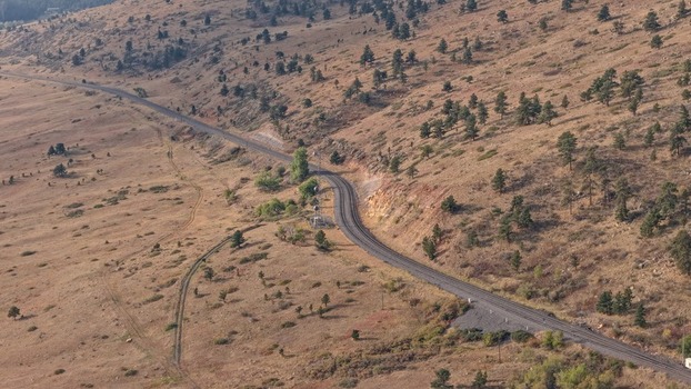 Aerial view of a railway track winding through the dry hilly landscape with scattered pine trees and rocky terrain in Golden Colorado United States.