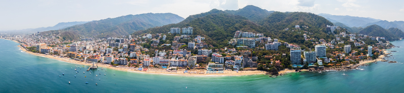 Aerial view of the city blending into lush verdant mountains overlooking a vibrant coastline dotted with boats Puerto Vallarta Jalisco Mexico.