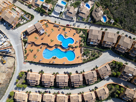 Aerial view of a residential complex with two interconnected swimming pools and terracotta tiled roofs surrounded by streets in Moraira Valencian Community Spain.