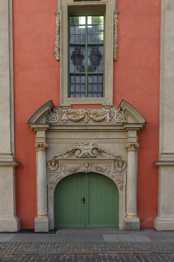 View of an ornate historic doorway with a green wooden door and intricate stone carvings set into a salmon colored building facade in Gdansk Pomeranian Voivodeship Poland. View of an ornate historic doorway with a green wooden door and intricate stone carvings set into a salmon colored building facade in Gdansk Pomeranian Voivodeship Poland.