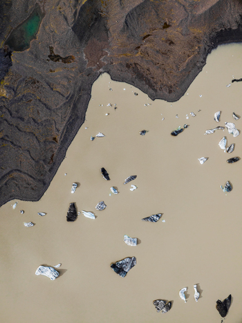 Aerial view of icebergs floating in a glacial lagoon with dark volcanic sediment and murky water in Iceland. Aerial view of icebergs floating in a glacial lagoon with dark volcanic sediment and murky water in Iceland.