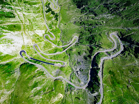 Aerial view of the winding Transfagarasan mountain road with sharp hairpin turns cutting through lush green slopes in Curtea de Arges Judetul Arges Romania. Aerial view of the winding Transfagarasan mountain road with sharp hairpin turns cutting through lush green slopes in Curtea de Arges Judetul Arges Romania.
