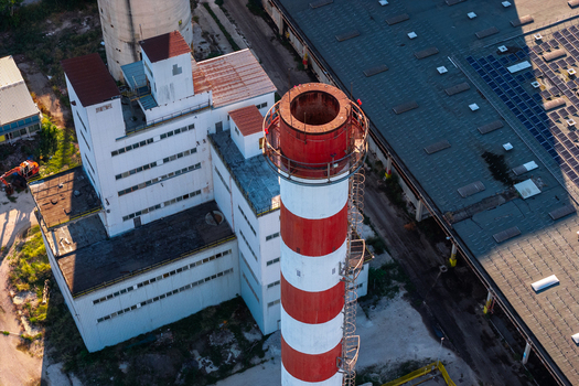 Aerial view of an industrial facility featuring a prominent red and white striped chimney a large white building and a warehouse with solar panels in Nera Montoro Umbria Italy. Aerial view of an industrial facility featuring a prominent red and white striped chimney a large white building and a warehouse with solar panels in Nera Montoro Umbria Italy.