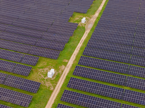 Aerial view of rows of solar panels in a field with a dirt path and electrical equipment in Poland.