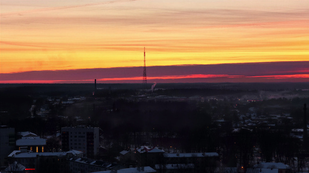 Aerial view of a town with snow covered rooftops and a tall communication tower silhouetted against a vibrant sunset sky in Latvia. Aerial view of a town with snow covered rooftops and a tall communication tower silhouetted against a vibrant sunset sky in Latvia.
