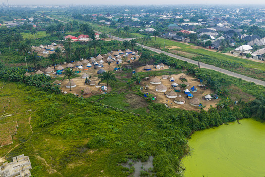 Aerial view of a settlement with traditional round huts and palm trees situated near a green pond in Port Harcourt Rivers State Nigeria. Aerial view of a settlement with traditional round huts and palm trees situated near a green pond in Port Harcourt Rivers State Nigeria.