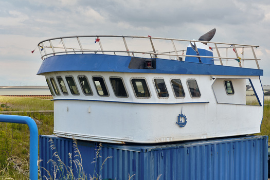 Den Oever Netherlands 18 May 2026 View of a boat cabin structure placed on a shipping container at the Machinefabriek fishing repair wharf under a cloudy sky.