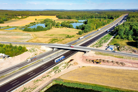 Aerial view of a highway overpass with trucks and cars driving through a rural landscape of fields and forests in Hochstadt Bavaria Germany. Aerial view of a highway overpass with trucks and cars driving through a rural landscape of fields and forests in Hochstadt Bavaria Germany.