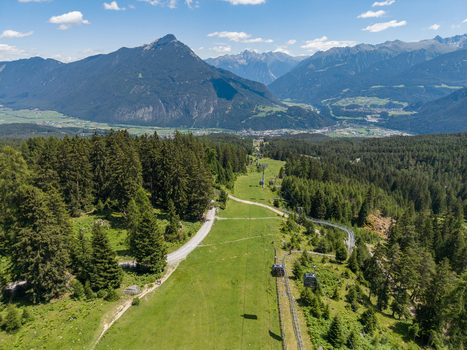 Aerial view of the Imst mountain resort in Tyrol Austria featuring a cable car line lush green meadows dense pine forests and a winding path Imst Tyrol Austria.