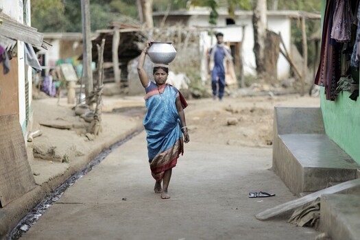 Odisha India 26 March 2026 View of a woman gracefully balancing a gleaming metal pot on her head her blue saree a vibrant splash against the earthy tones of the rural street. Odisha India 26 March 2026 View of a woman gracefully balancing a gleaming metal pot on her head her blue saree a vibrant splash against the earthy tones of the rural street.