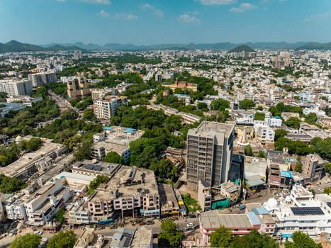Aerial view of the cityscape of Udaipur featuring dense urban development residential buildings lush green trees and distant hills in Udaipur Rajasthan India.
