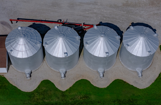 Aerial view of four metallic grain silos arranged in a row on a farm with green grass and gravel ground in Lakeshore Ontario Canada. Aerial view of four metallic grain silos arranged in a row on a farm with green grass and gravel ground in Lakeshore Ontario Canada.