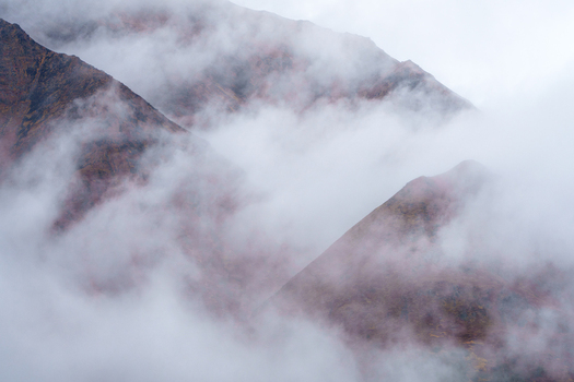 Aerial view of Denali Highway mountain slopes partially obscured by thick fog and low clouds in the wilderness of Cantwell Alaska United States.
