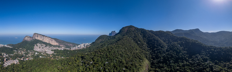 Aerial view of Parque Florestal da Tijuca featuring dense tropical rainforest covering mountainous terrain with distant urban buildings and coastline in Rio de Janeiro Rio de Janeiro Brazil.