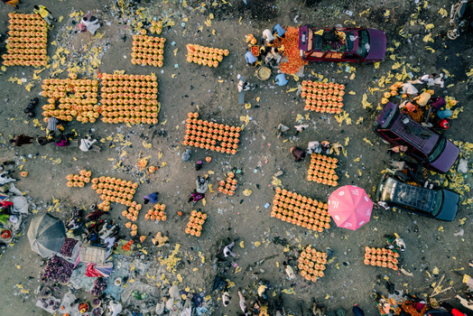 Aerial view of Panteka Market with people sorting produce in yellow crates parked vehicles and a pink umbrella on the dusty ground Kaduna Kaduna Nigeria. Aerial view of Panteka Market with people sorting produce in yellow crates parked vehicles and a pink umbrella on the dusty ground Kaduna Kaduna Nigeria.